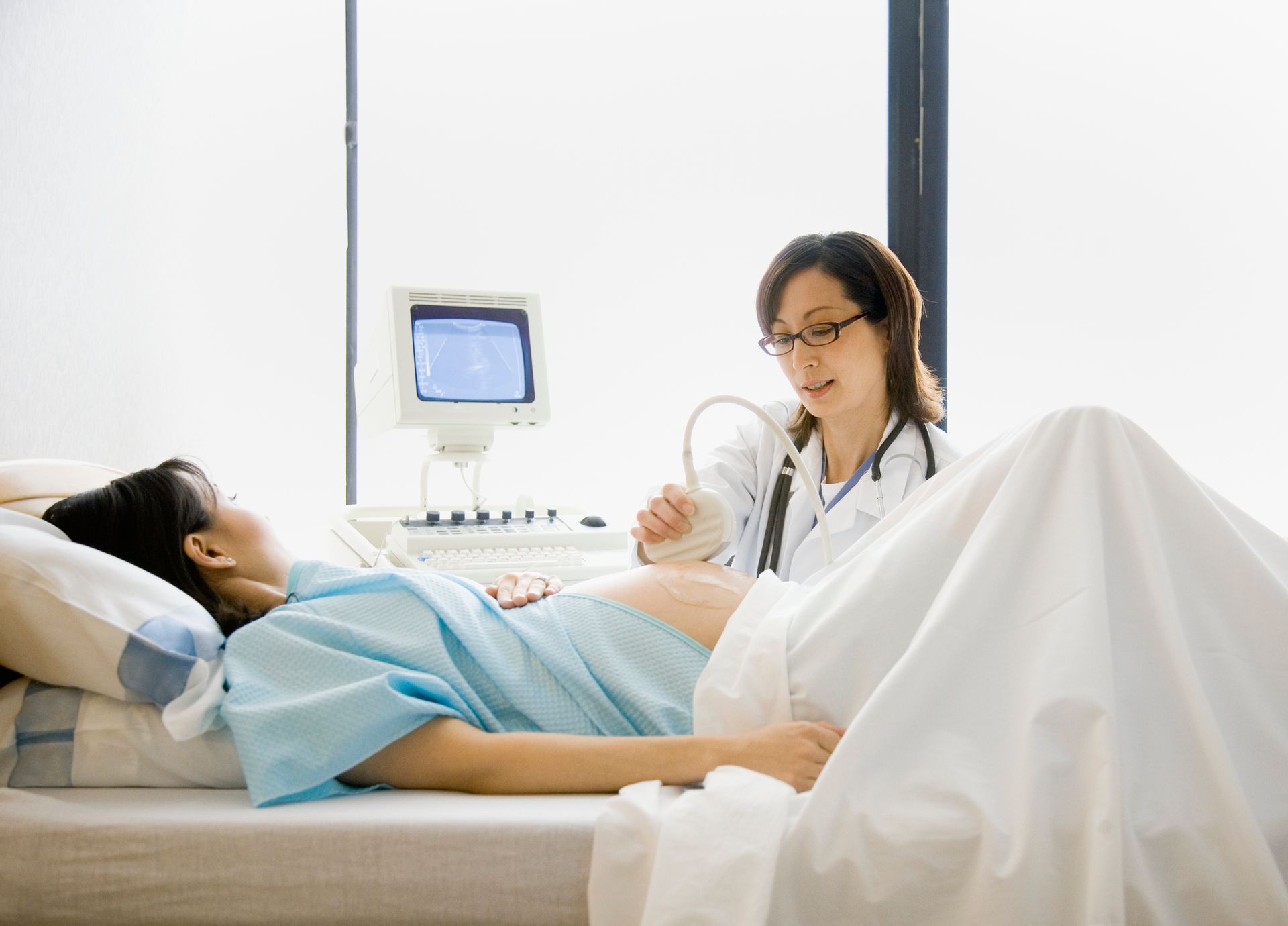 A pregnant woman is laying in a hospital bed while a doctor examines her belly.