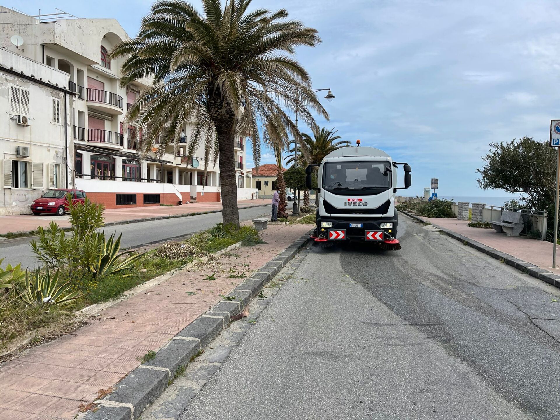 Camion parcheggiato su una strada costiera accanto a palme ed edifici bianchi.