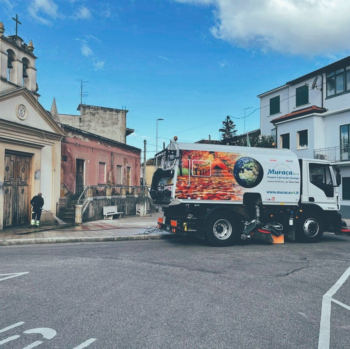 Scena di strada con un camion bianco e fiamme arancioni in una piazza cittadina sotto un cielo azzurro.