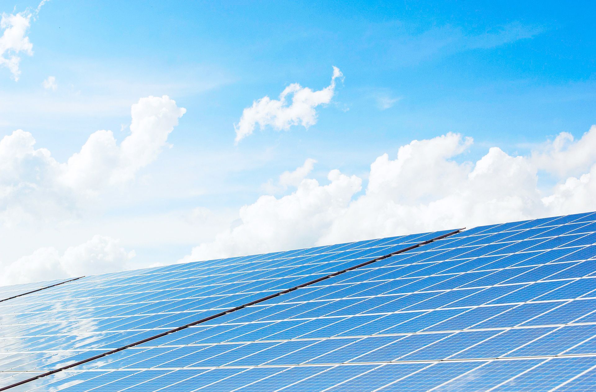 Solar panels stretching toward a bright blue sky with scattered white clouds