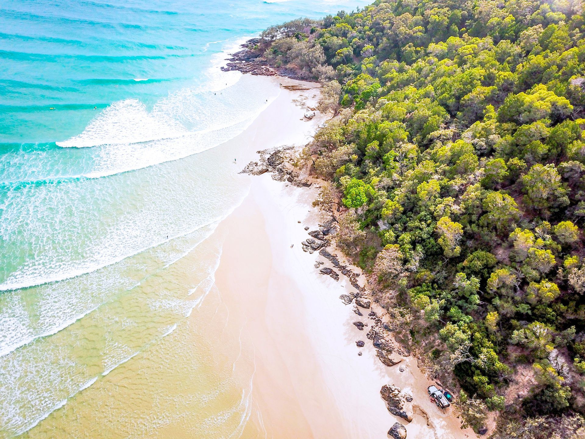 Aerial view of a turquoise shoreline with white sand and dense green trees along the coast
