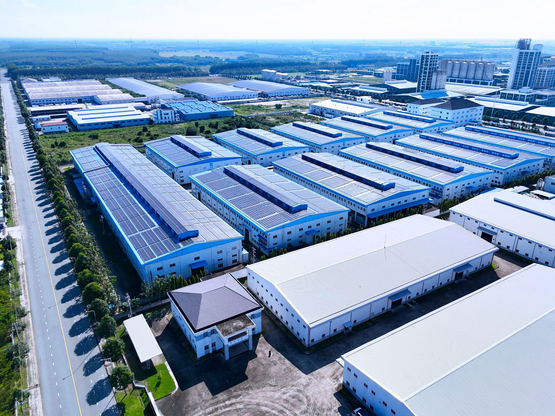 Aerial view of a large blue-and-white industrial warehouse complex with roads and trucks nearby