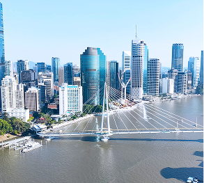 Modern city skyline with a cable-stayed bridge over a wide river on a sunny day