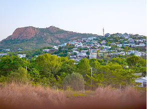 Hillside town with white houses, green trees, and a rocky mountain under a clear sky