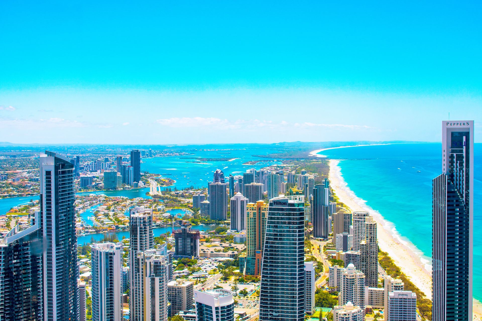 Sunny coastal skyline with tall high-rises beside a turquoise ocean and white sandy beach
