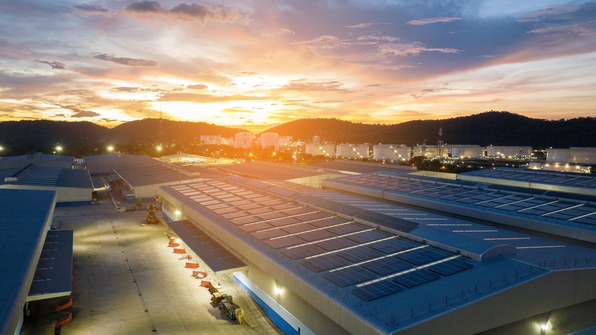 Sunrise over a large solar-panel-covered industrial facility with mountains in the background