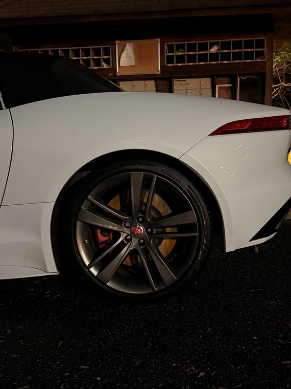 Rear side view of a white sports car with large alloy wheel parked at night in front of a building.