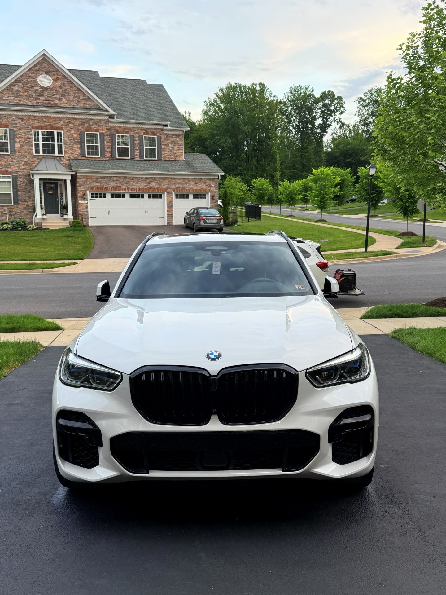 White BMW SUV parked on a suburban street in front of a brick house and trees