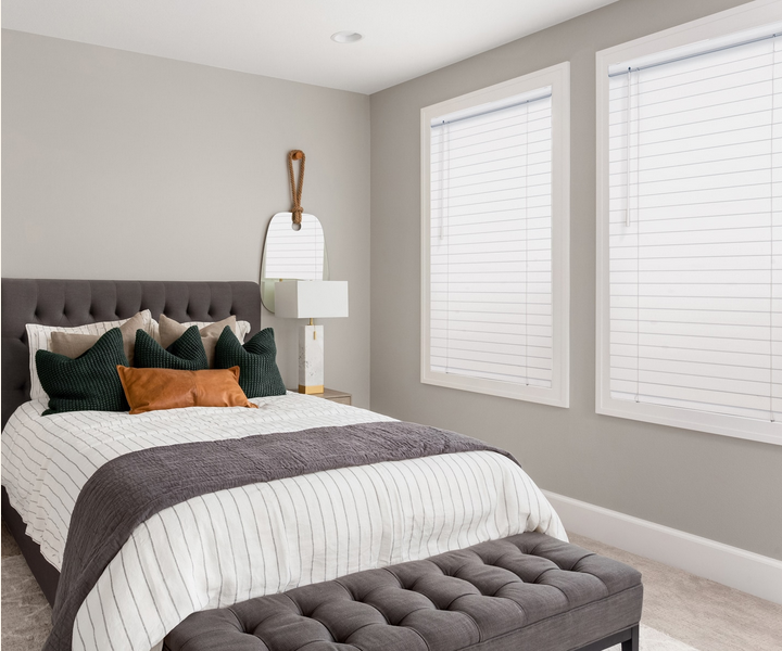 a bedroom with a bed , two windows with faux wood blinds and a bench All Window Decor (817) 448-3393.