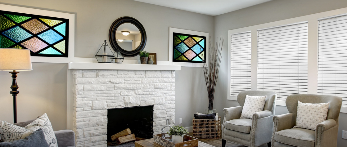 a living room with a fireplace , chairs , a lamp and stained glass windows and faux wood blinds on the windows All Window Decor (817) 448-3393 .