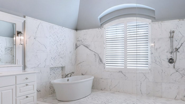 a bathroom with a tub , sink , mirror and shower with shutters All Window Decor (817) 448-3393.