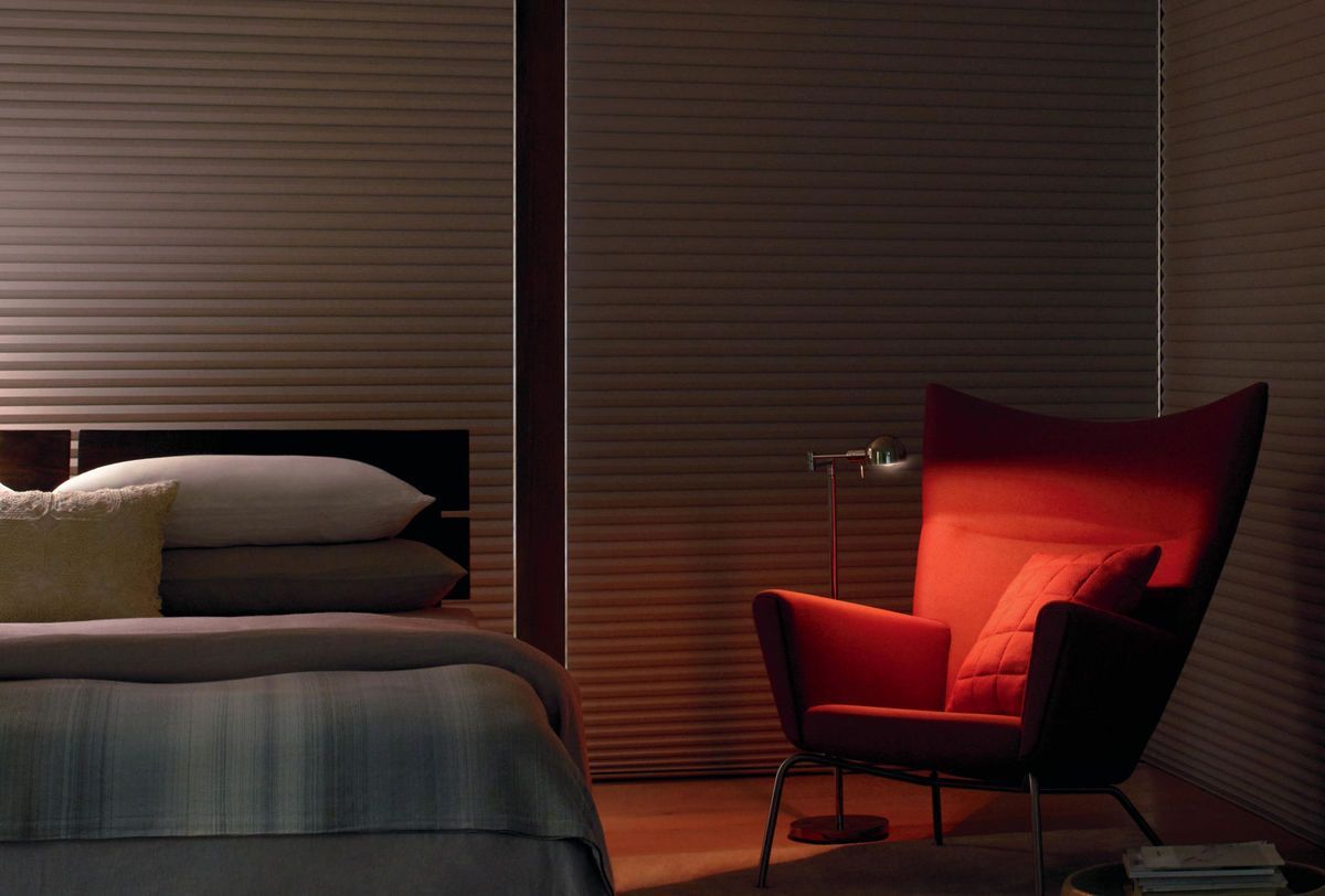 a bedroom with a bed and a red chair with blackout honeycomb shades All Window Decor (817) 448-3393
