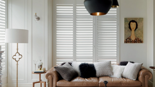 a living room with a brown couch and white shutters on the windows All Window Decor (817) 448-3393.