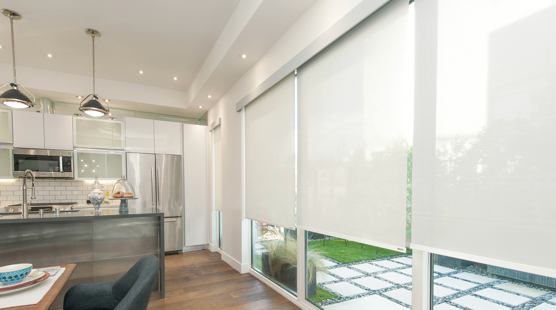 a kitchen and dining room with white roller shades on the windows All Window Decor (817) 448-3393.