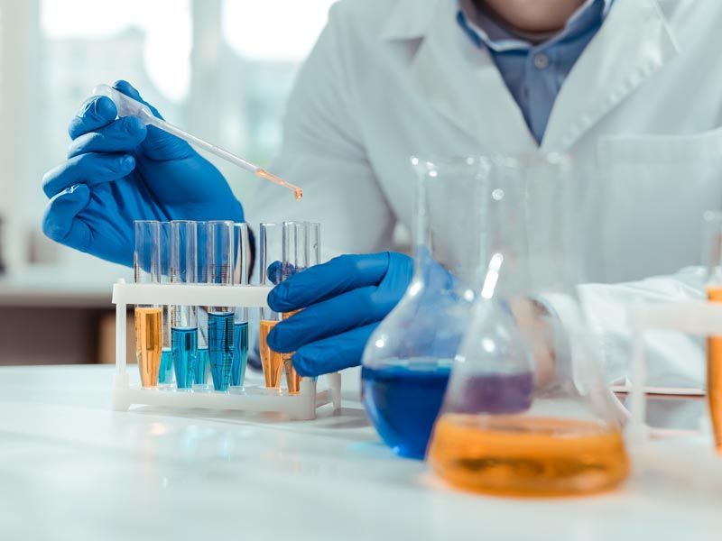 Scientist in blue gloves handling test tubes and flasks in a laboratory