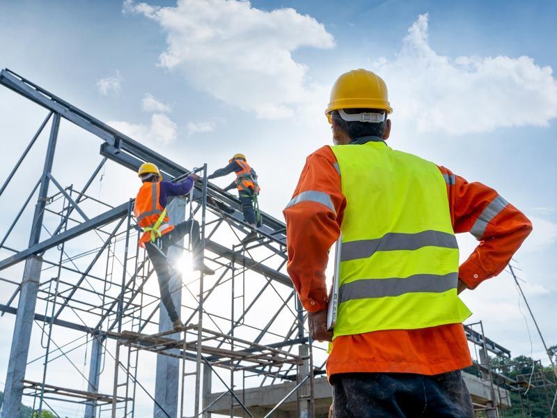 Construction workers in orange and yellow safety gear assembling a steel structure outdoors