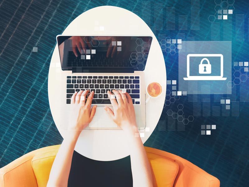 Hands typing on a laptop with a security lock icon on screen against a blue digital background