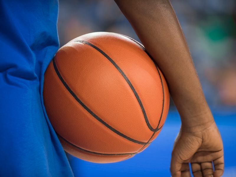 Basketball held at a player’s side on a court, with a blue jersey visible.