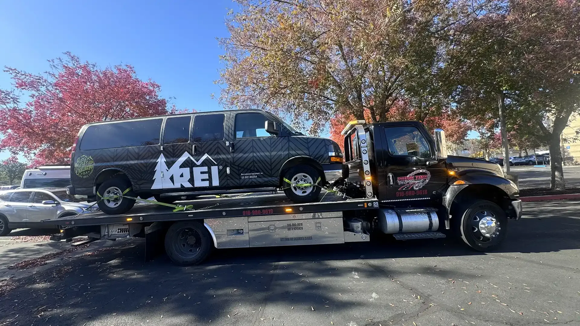 A tow truck is carrying a van that says rei on it.