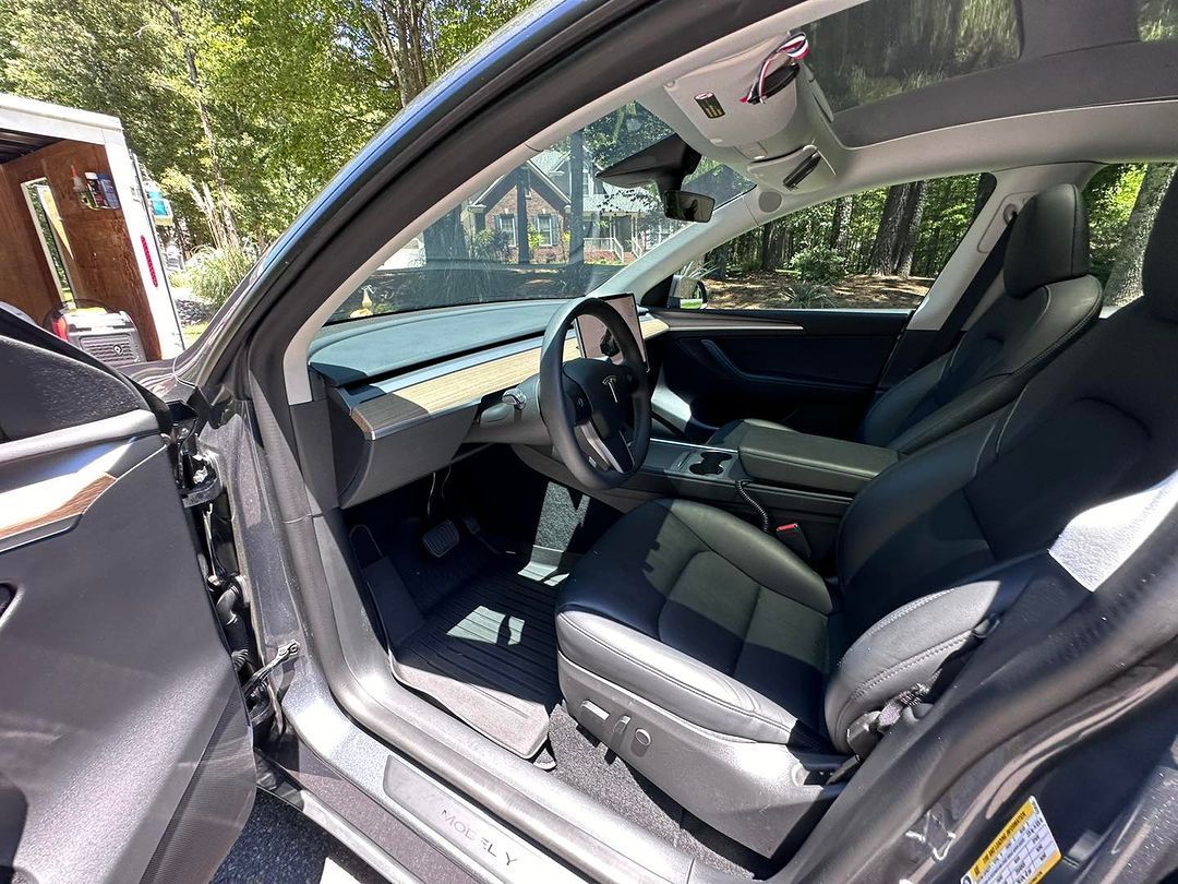 Open car door showing a black interior with front seat and steering wheel in daylight