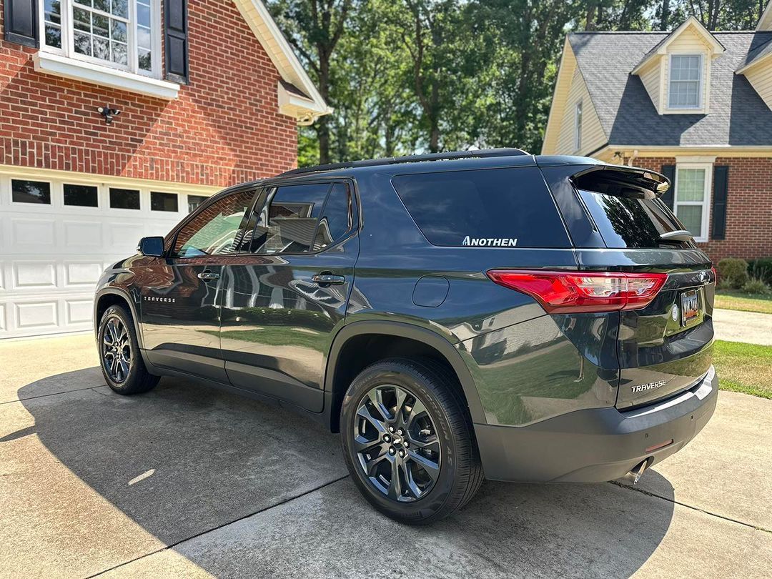 Dark green SUV parked in a driveway beside a house and garage in a suburban neighborhood