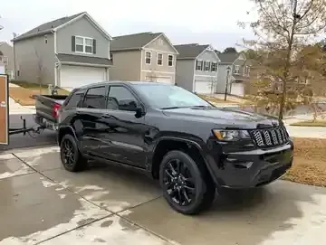 Black SUV parked in a suburban driveway beside houses on a cloudy day