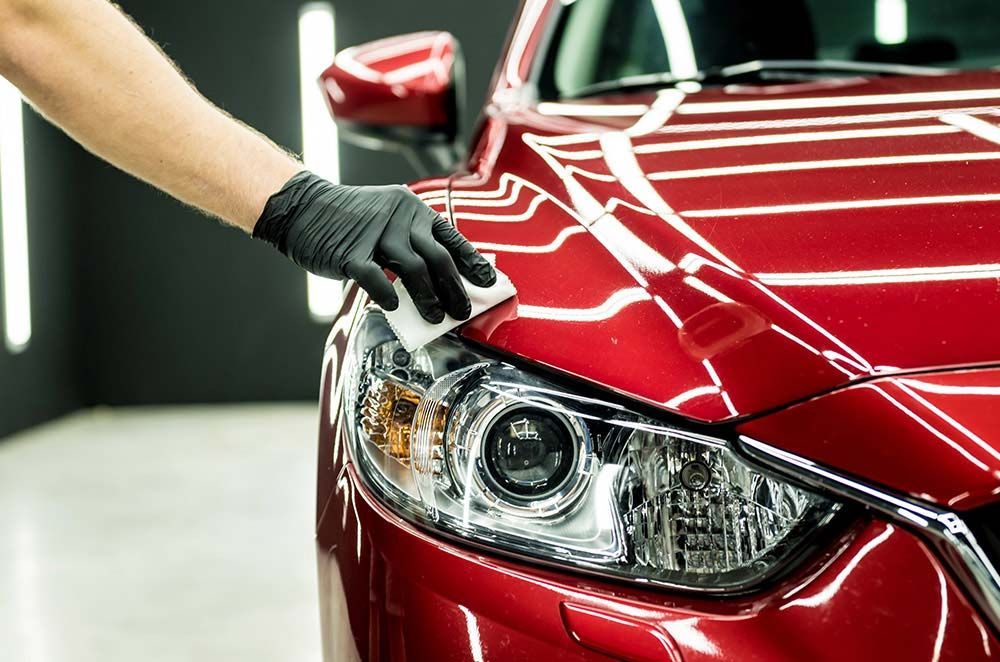 Gloved hand polishing the headlight of a red car in a garage