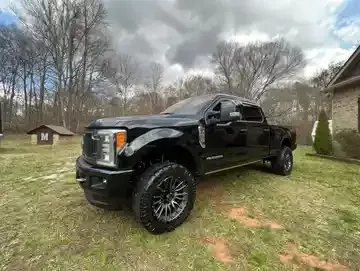 Black pickup truck parked on grass beside a house under cloudy sky