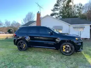 Black SUV parked on grass in front of a white house with a brick chimney