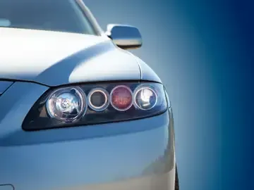 Close-up of a silver car’s front headlight assembly with blue reflections