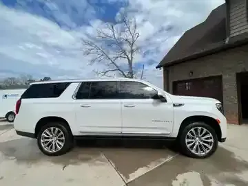 White SUV parked beside a brick house on a driveway under a cloudy sky.