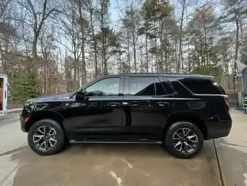 Black SUV parked on a wet driveway in front of bare trees and houses