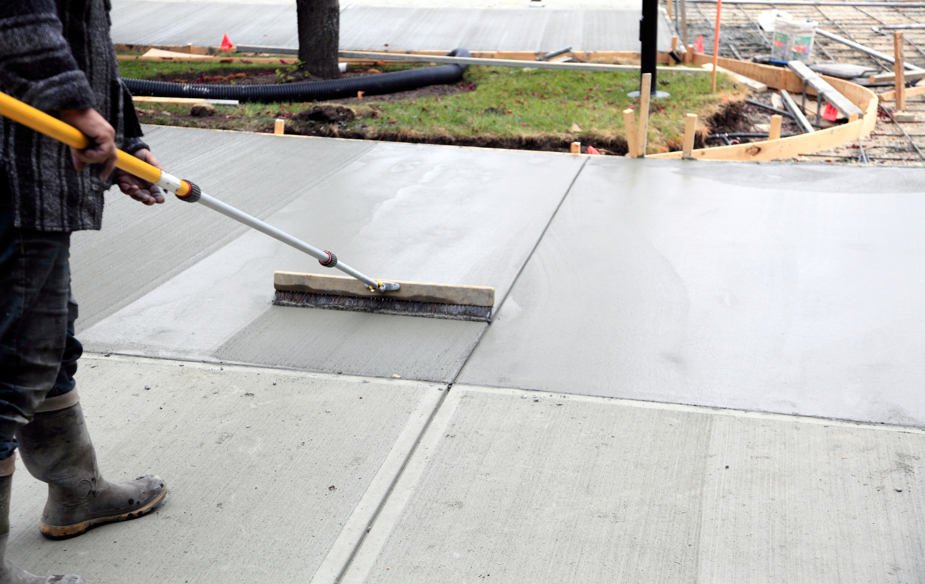 A man is spreading concrete on a sidewalk with a broom.