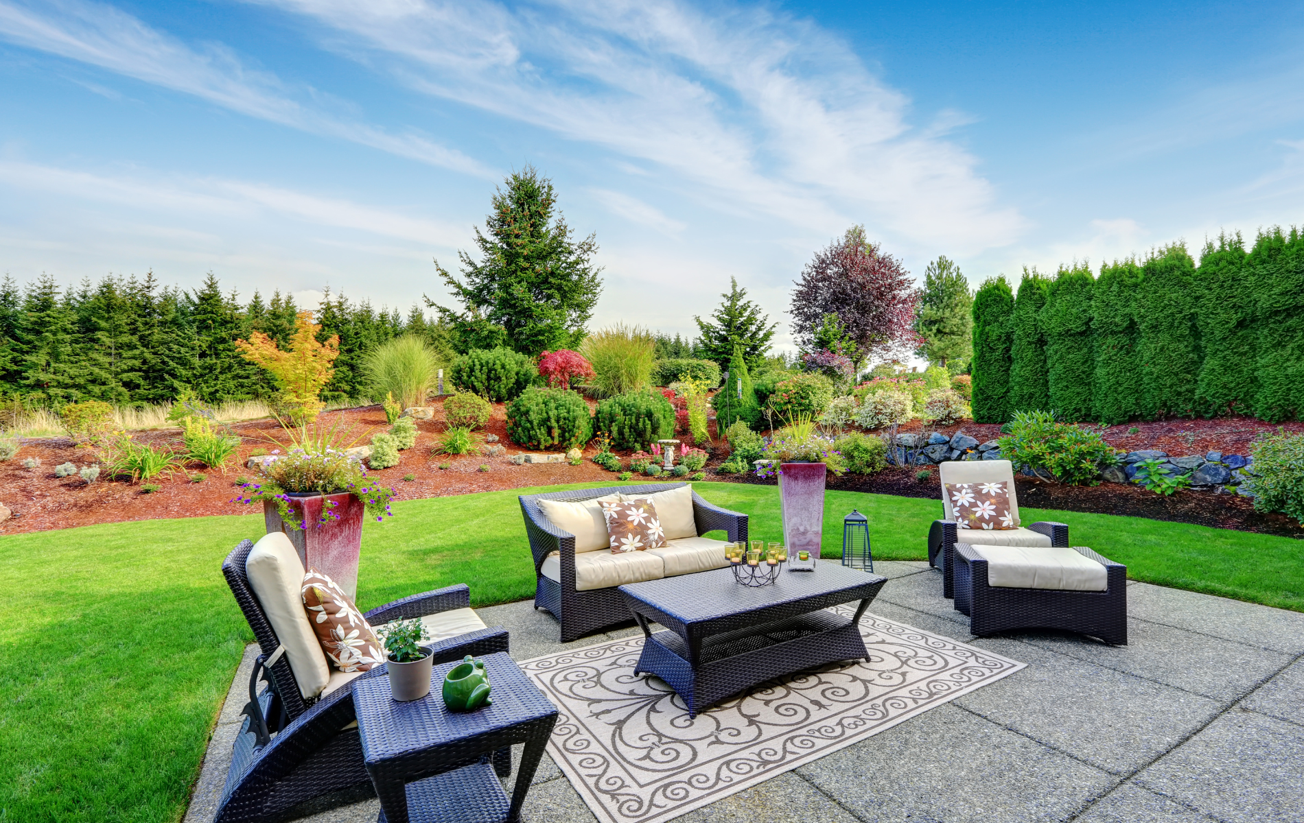 A patio with a couch , chairs , table and rug in a backyard.