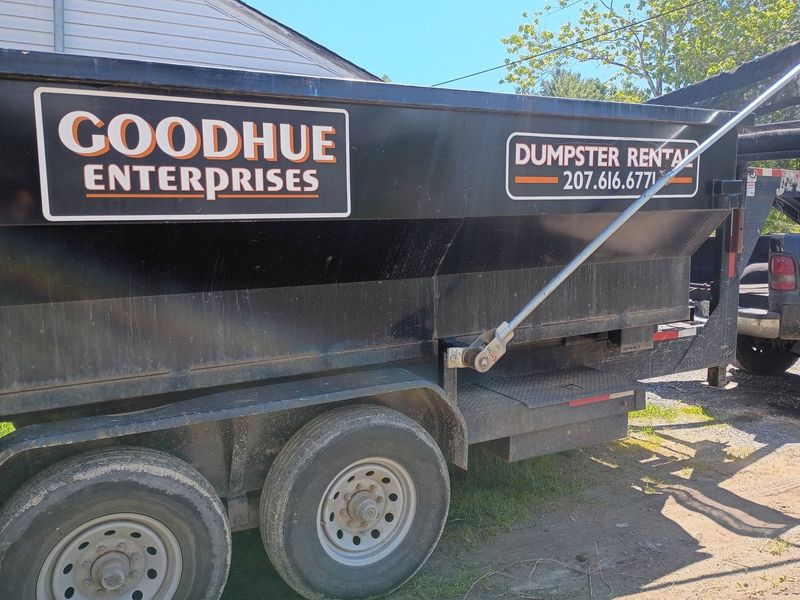 Black Goodhue Enterprises dumpster rental trailer parked outdoors with phone number on side.
