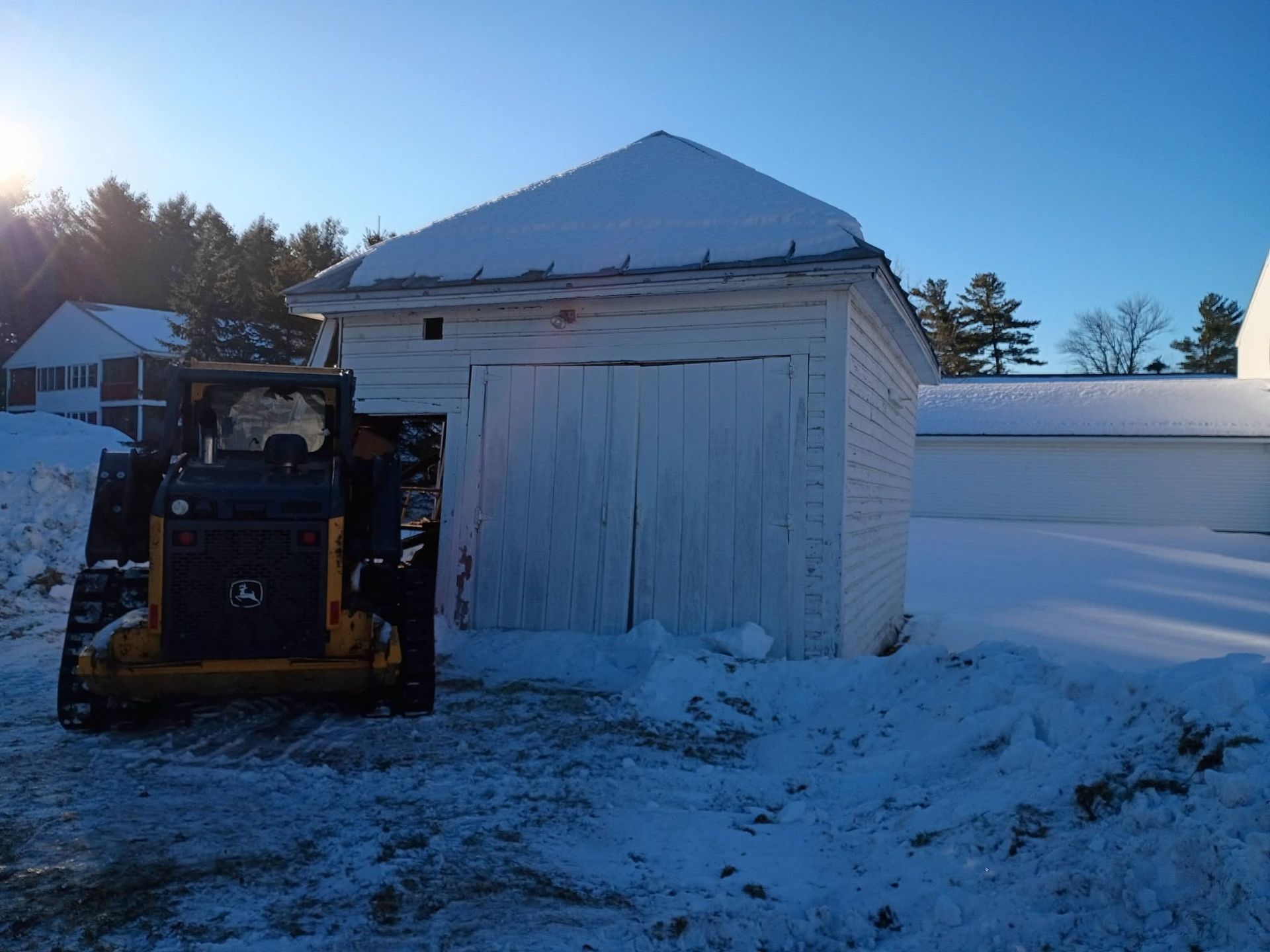 Snowy yard with a white shed and a black snowplow clearing snow in front.