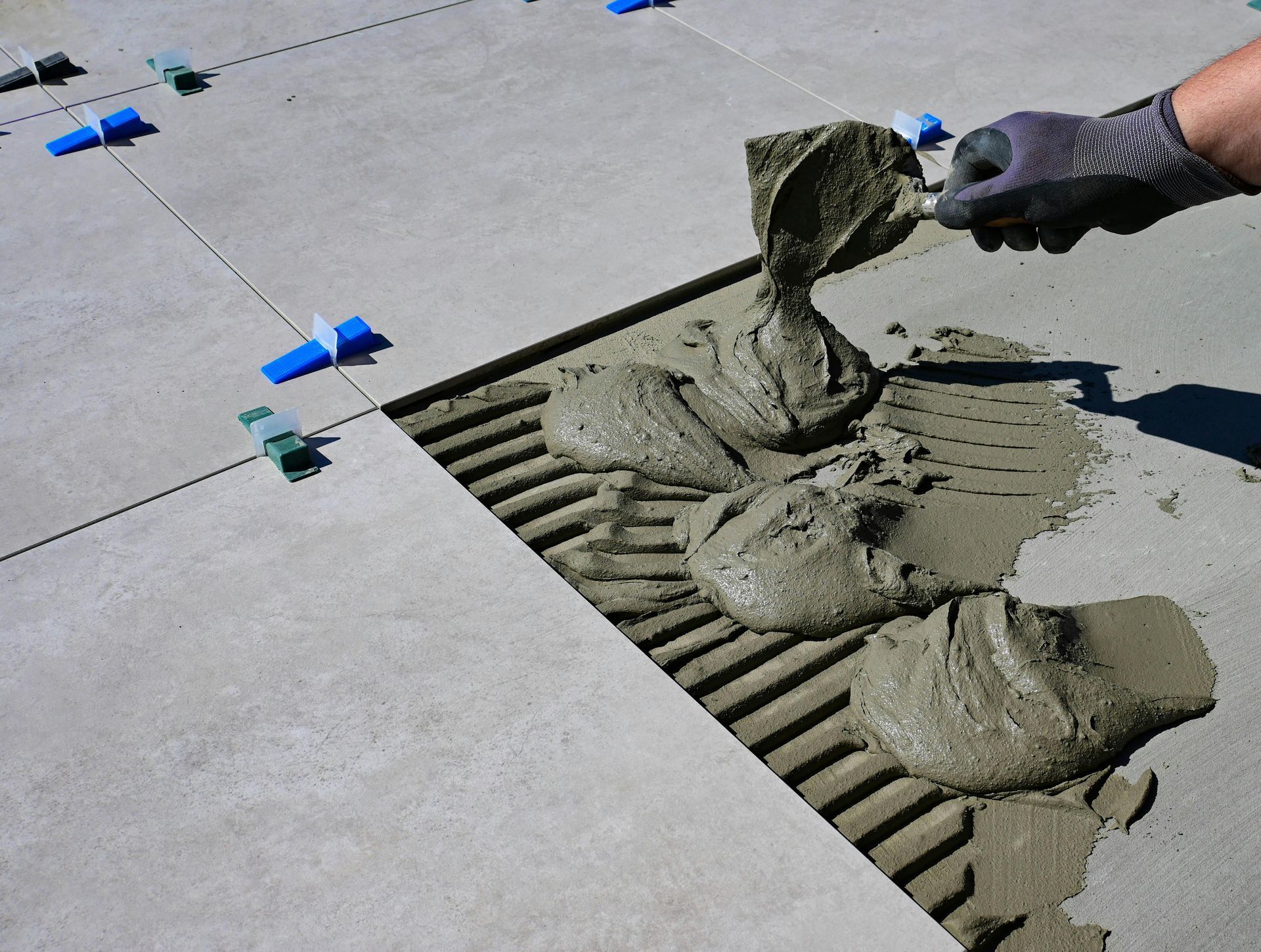 Worker Spreading Wet Concrete Over A Floor Repair Joint Near Blue Tape Markers — Lunny's Carpentry In Dubbo, NSW