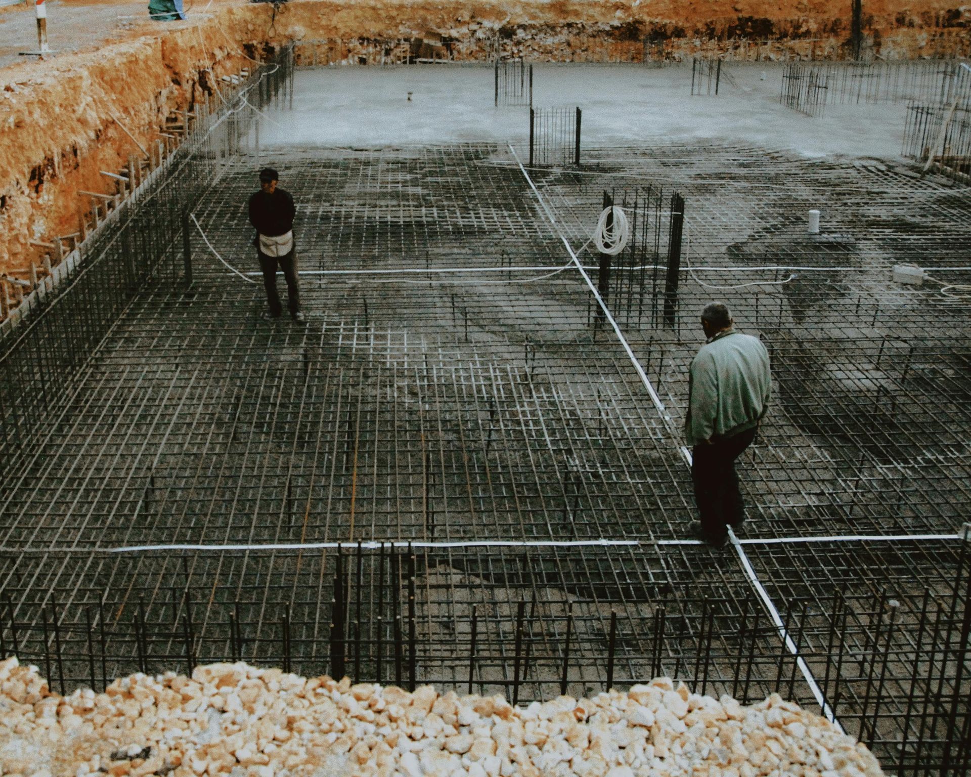 Workers Standing In A Concrete Foundation Pit With Steel Rebar Grid And Stone Walls — Lunny's Carpentry In Dubbo, NSW