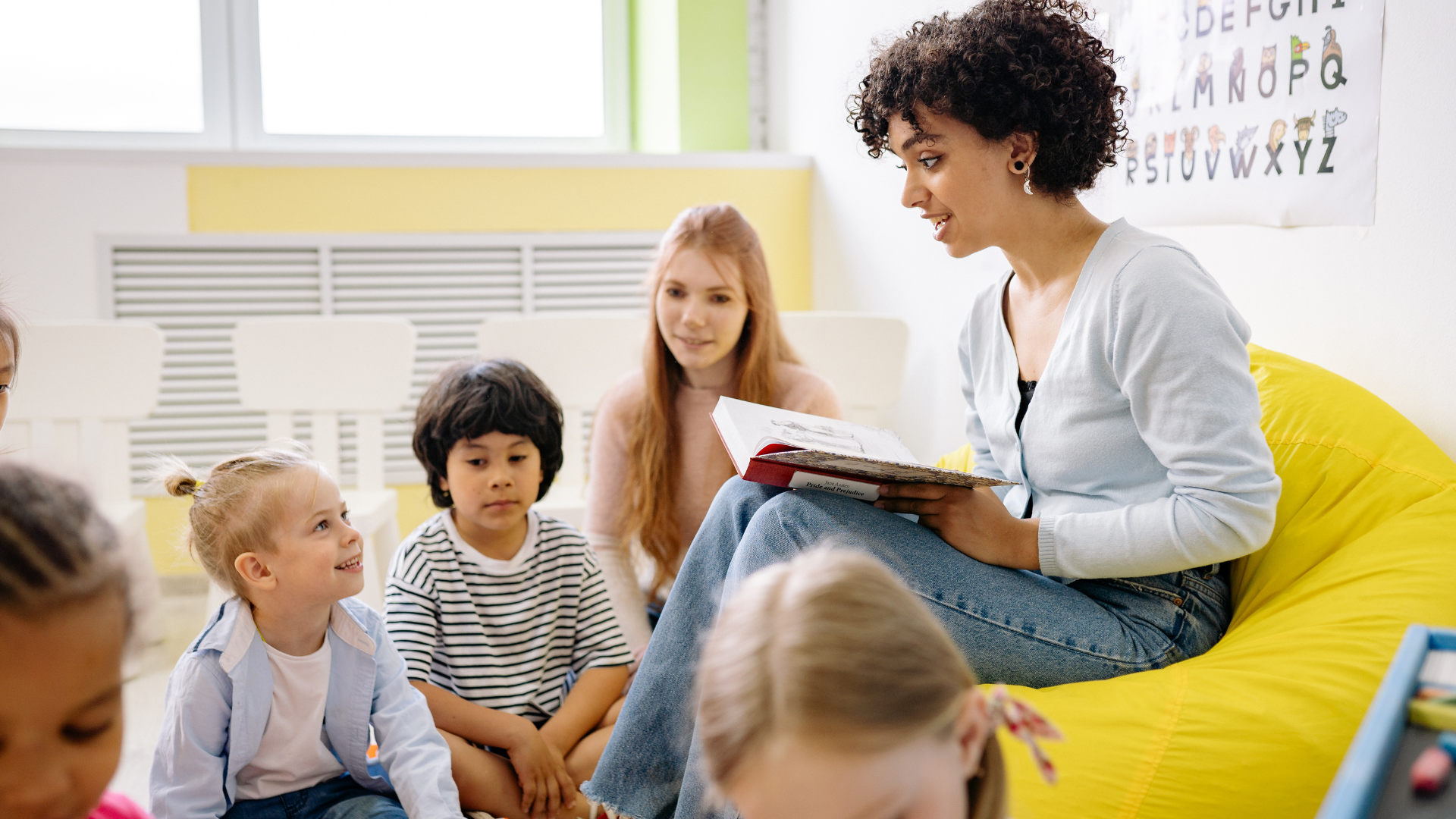 A woman is sitting on a bean bag chair reading a book to a group of children.