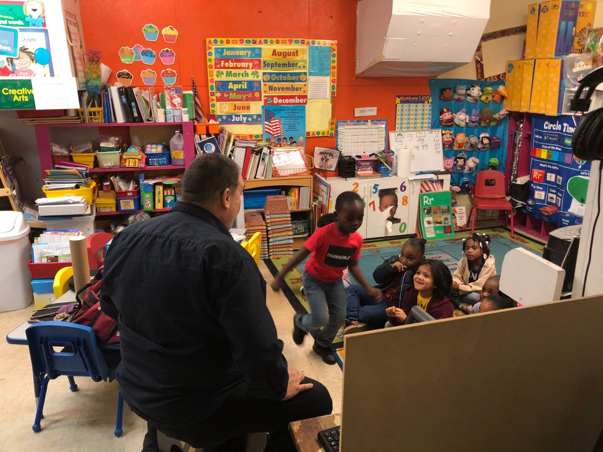 A man is sitting in front of a group of children in a classroom.