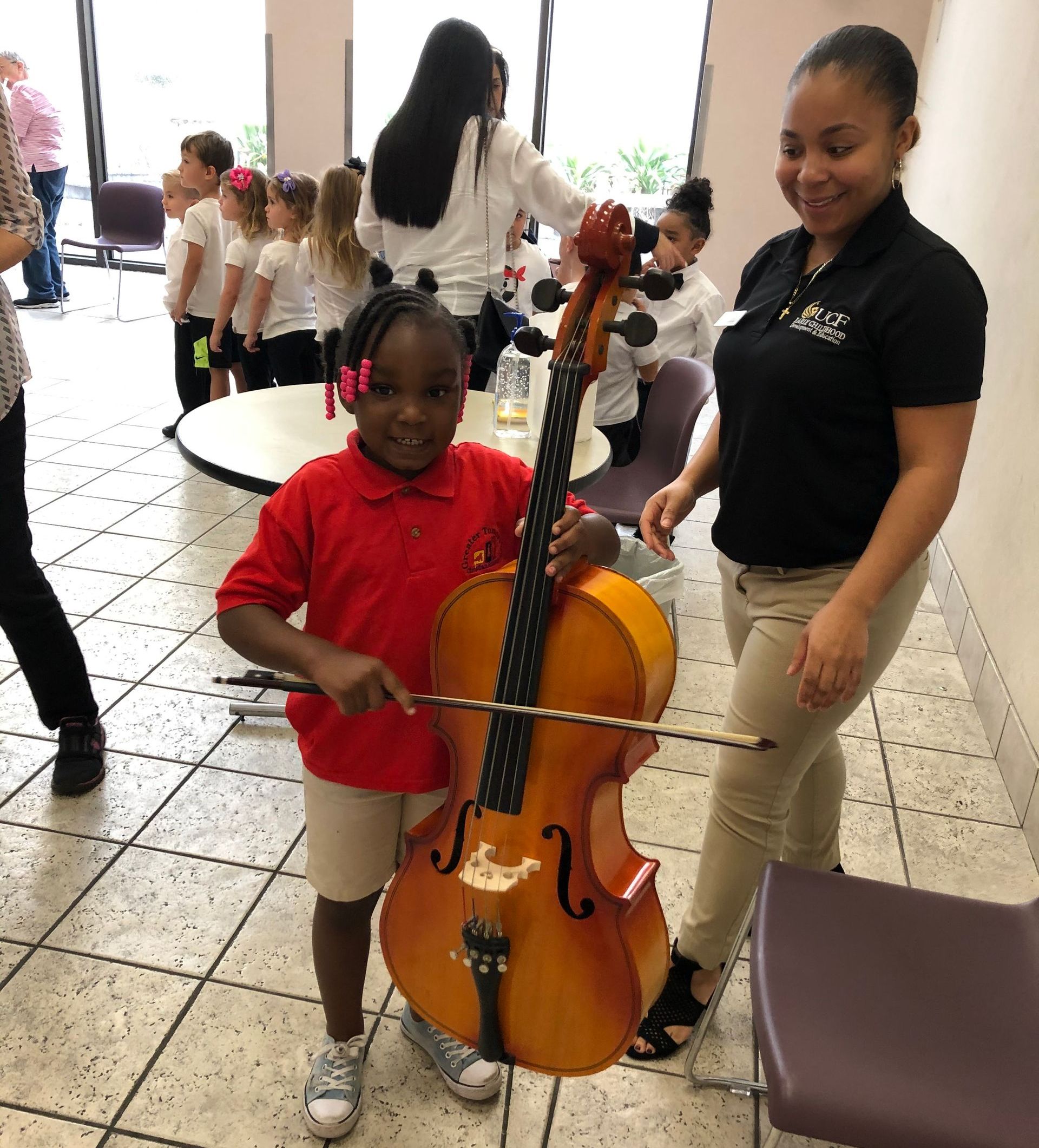 A girl in a red shirt is holding a cello