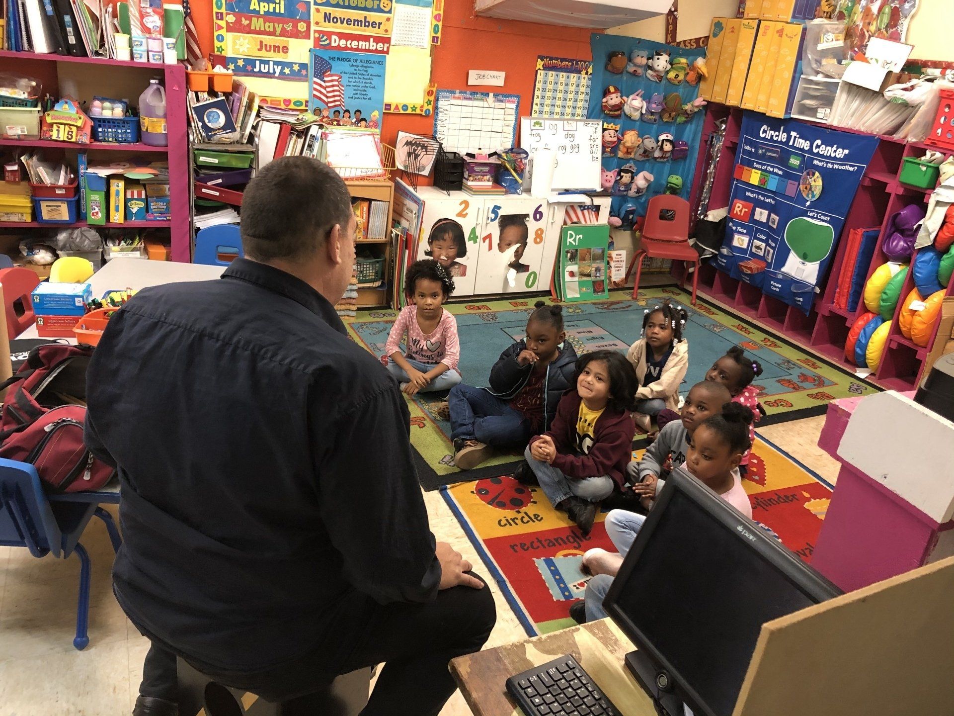 A man is sitting in front of a group of children in a classroom.