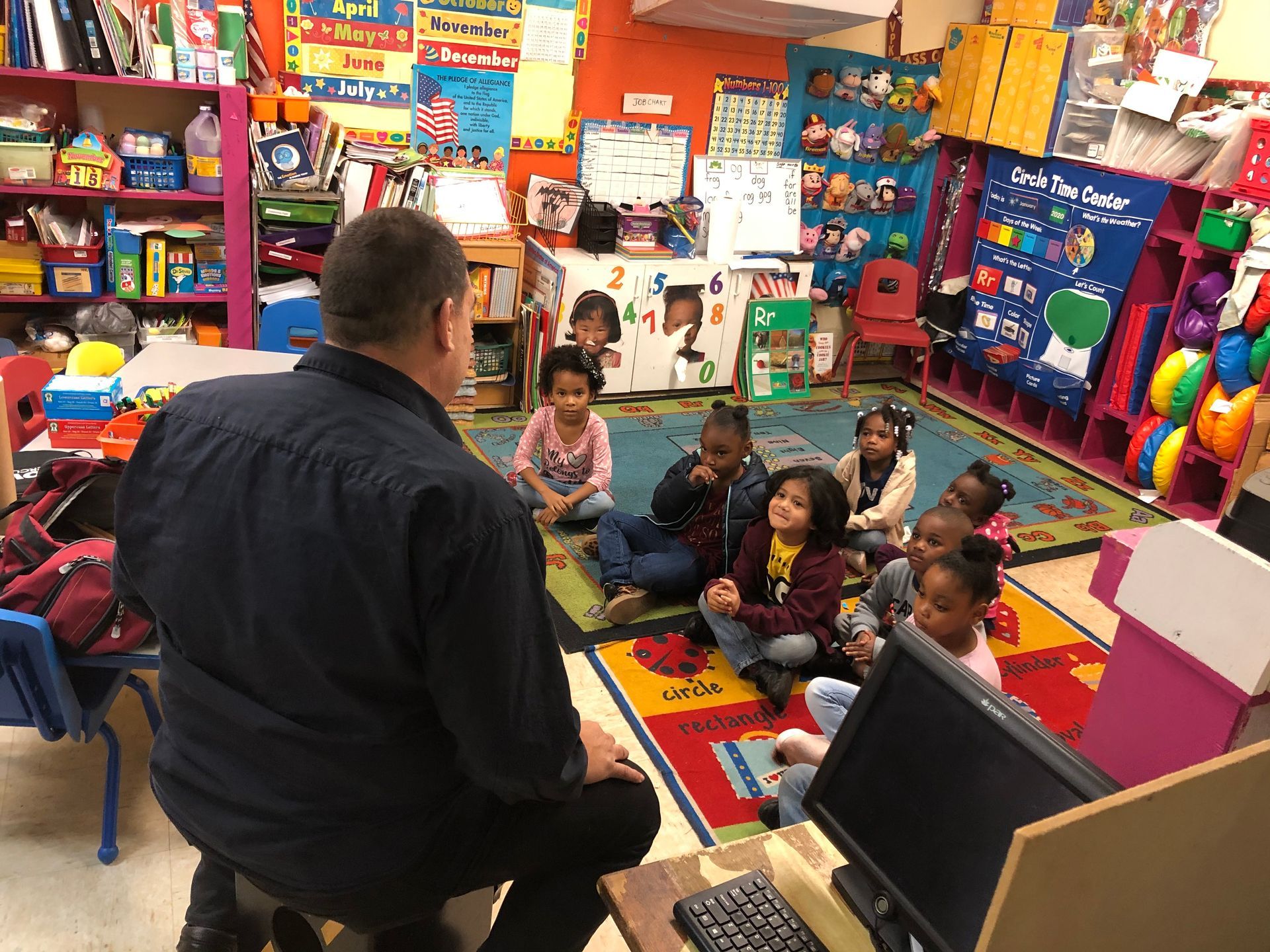A man is sitting in front of a group of children in a classroom.