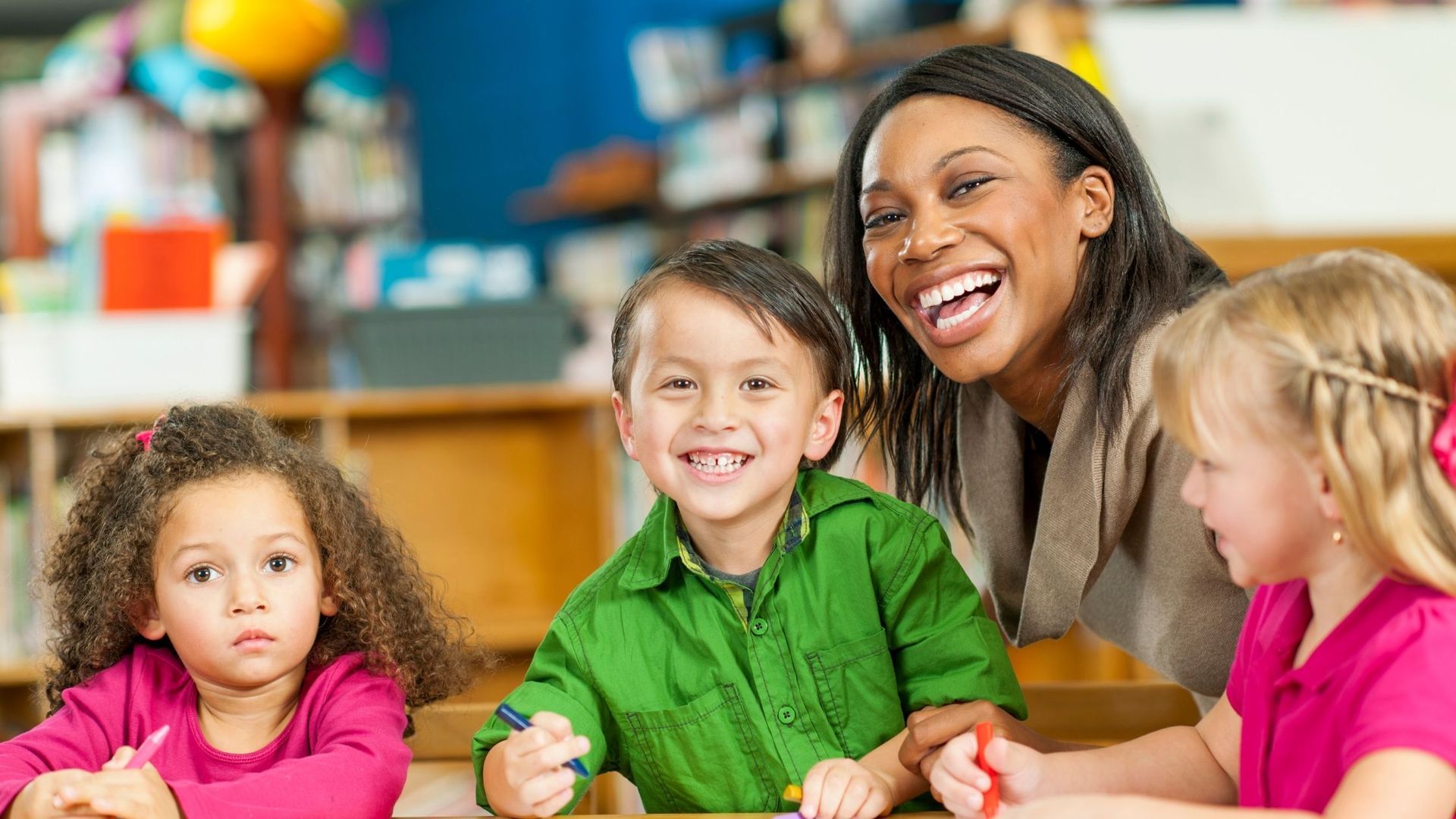 Teacher and children smiling together in classroom.