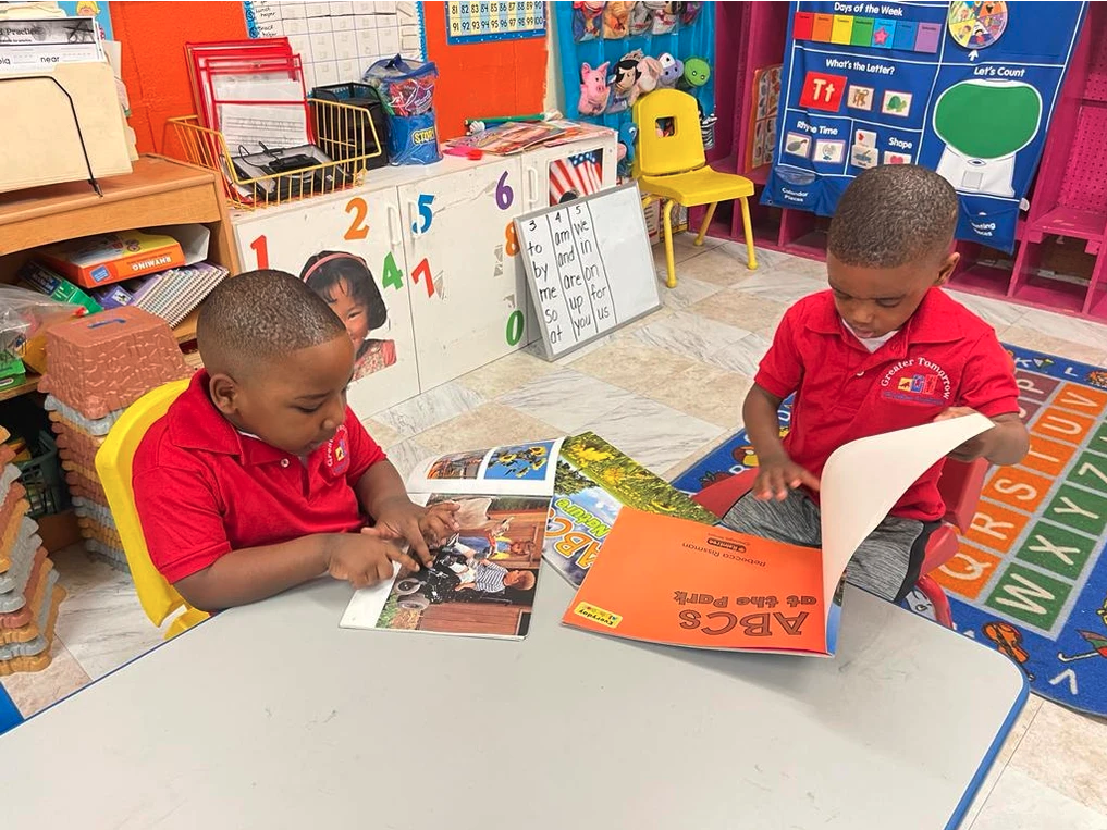 Two young boys are reading books in a classroom.