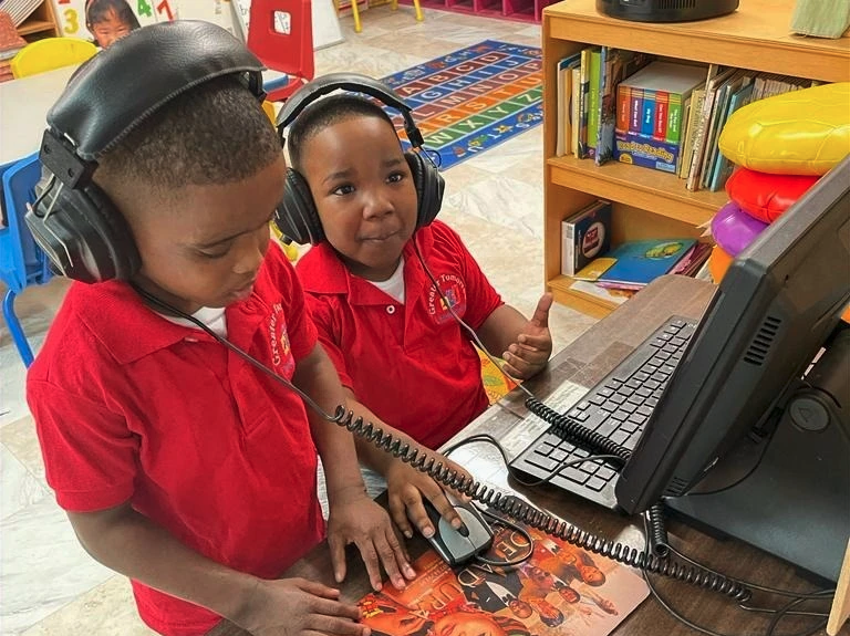 Two young boys wearing headphones are looking at a computer screen.
