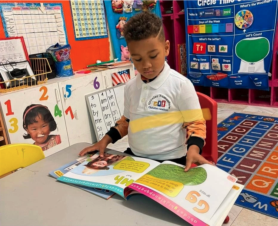 A young boy is reading a book in a classroom.