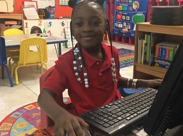 A little girl in a red shirt is using a computer