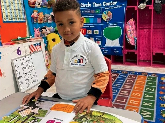 A young boy is reading a book in a classroom with a sign that says circle time center