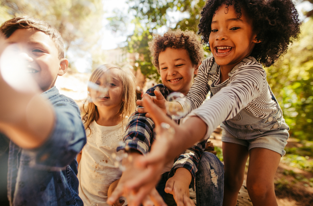 A group of children are giving each other a high five while blowing soap bubbles.
